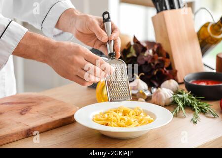 Male chef grating garlic into plate with pasta in kitchen, closeup Stock Photo