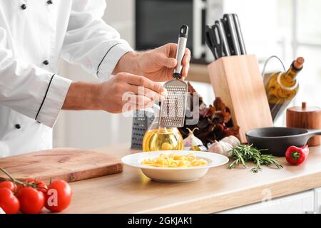 Italian chef grating garlic into pasta in kitchen, closeup Stock Photo