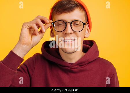 guy has poor eyesight, a handsome guy in an orange hat and red light and glasses for vision squints, on a yellow background Stock Photo