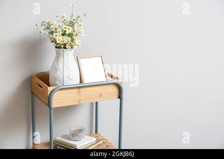Vase with chamomiles and frame on shelf near light wall Stock Photo