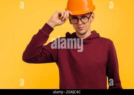 handsome man in a construction helmet and a goggle, young student builder, choosing a profession for a student, holding an orange helmet with his hand Stock Photo