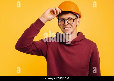 handsome man in a construction helmet and a goggle, young student builder, choosing a profession for a student, holding an orange helmet with his hand Stock Photo