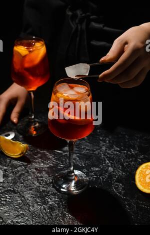 Female bartender preparing tasty aperol spritz cocktail on dark background, closeup Stock Photo