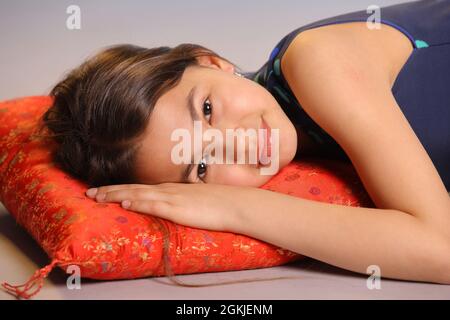 Portrait of an adorable dark-haired teenage girl 12 years old. She lies on a red pillow and smiles. Stock Photo