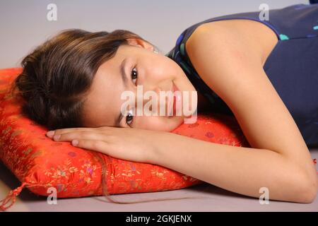 Portrait of an adorable dark-haired teenage girl 12 years old. She lies on a red pillow and smiles. Stock Photo