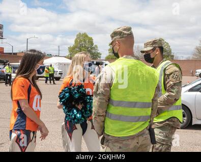U.S. Army Sgt. James Hines, middle right, and U.S. Army Pfc. Eloy Martinez, far right, cavalry scouts assigned to 3rd Squadron, 61st Calvary Regiment, speak with cheerleaders of the Denver Broncos at the Community Vaccination Center (CVC) at the Colorado State Fairgrounds in Pueblo, Colorado, May 4, 2021. The Denver Broncos mascot and cheerleaders visited the Pueblo CVC to support Soldiers and community members. U.S. Northern Command, through U.S. Army North, remains committed to providing continued, flexible Department of Defense support to the Federal Emergency Management Agency as part of t Stock Photo