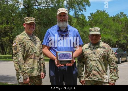 US Army Sgt. 1st Class Matthew Pennington, a counterintelligence agent (left), and Command Sgt. Maj. Michael R. Mabanag (right), both with the 504th Expeditionary Military Intelligence Brigade, presents Gary Wilder, Pennington’s former drill sergeant (center), with a gift in Lions Park, Temple, Texas on May 7, 2021. The gift is a picture of Pennington’s basic training class. Stock Photo