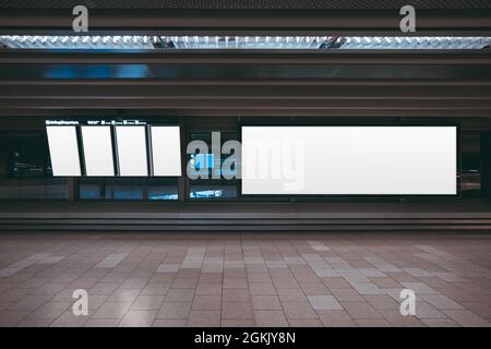 A huge rectangular empty billboard mockup in an airport departure area with vertical LCD screens mock-ups; a white blank poster template indoors of a Stock Photo