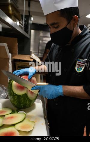 SAN DIEGO (May 11, 2021) Culinary Specialist Seaman Khatiwada Ran, from Kathmandu, Nepal, cuts watermelon aboard amphibious assault ship USS Essex (LHD 2), May 11. Sailors and Marines of the Essex Amphibious Ready Group (ARG) and the 11th Marine Expeditionary Unit (MEU) are underway off the coast of southern California. Stock Photo