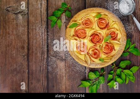 Apple shaped like roses on tart on rustic wooden table. Stock Photo