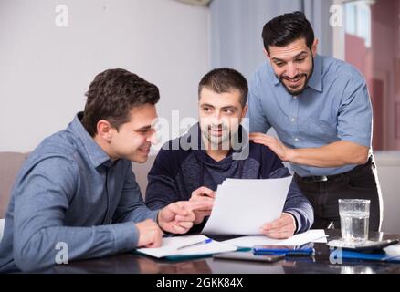 Three smiling men discussing papers at desk Stock Photo