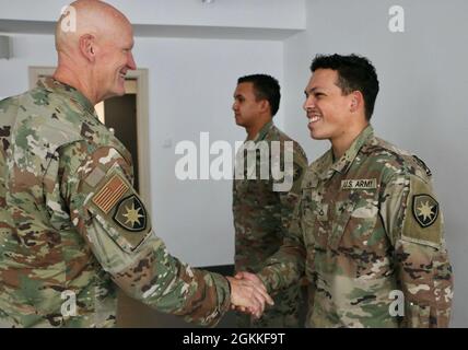 Air Force Maj. Gen. James Eifert (left), Florida National Guard adjutant general, presents Army Pfc. Josue Luna (right) and Spc. Kenneth Eprestalvo (center) with a coin in a handshake to recognize their excellent performance at Forward Operating Site (FOS) Drawkso Pomorskie Training Area, Poland, on May 15, 2021. Eifert thanks the Soldiers and emphasizes the importance of their roles during their deployment. Luna and Esprestalvo are assigned to the 50th Regional Support Group from Homestead, Florida, which is deployed to Poland to support Atlantic Resolve by providing management and base opera Stock Photo