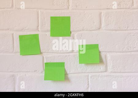 There are several green sticky notes hanging on the white brick wall Stock Photo