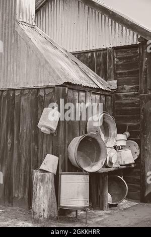 Old wooden hut with buckets, tubs and other containers hanging on the rough exterior wall in monotone Stock Photo