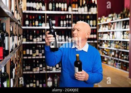 Attentive pensioner chooses red wine in a liquor store Stock Photo
