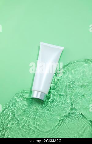 White bottle cosmetic tubes on the green water surface texture with ripples. Blank label for branding mock-up. Summer water pool fresh concept. Flat l Stock Photo