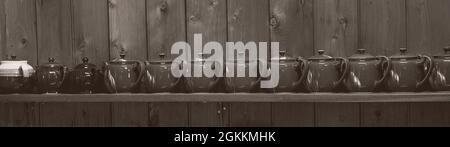 A row of little brown teapots all in a row on a shelf against a timber wall - monotone image Stock Photo