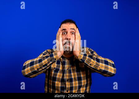 Young man with a frightened pose over blue monochrome background Stock Photo