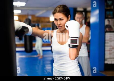 Asian female practicing punches with boxing bag at gym Stock Photo