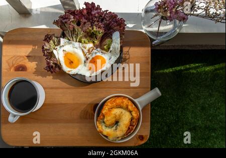 Breakfast with Spinach brioche, Two fried eggs, Oak Leaf lettuce served with Black coffee on wooden table at balcony. Selective focuse. Stock Photo