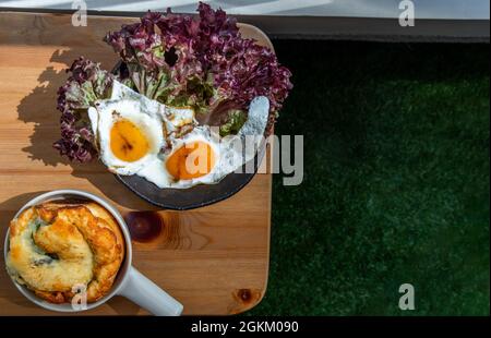 Breakfast with Spinach brioche, Two fried eggs, Oak Leaf lettuce on wooden table at balcony. Selective focuse. Stock Photo