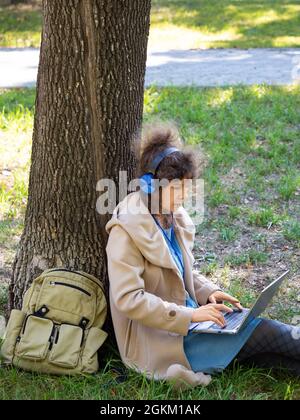 Vertical photo of a middle aged woman with laptop in city park. Online working or online education concept. Stock Photo
