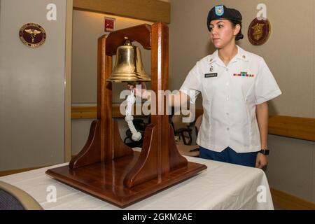 U.S. Army Spc. Aly Martinez, Naval Medical Research Unit-San Antonio animal care specialist, uses a bell to signal the arrival of the official party at the NAMRU-SA change of command ceremony at Brooke Army Medical Center, Joint Base San Antonio-Fort Sam Houston, Texas May 21, 2021. In Navy tradition the bell aboard a ship is rung to declare the changing of the watch but currently it is also used to announce the arrival and departure of visiting dignitaries. Stock Photo