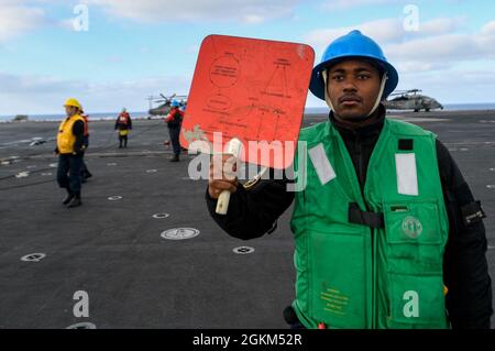 PACIFIC OCEAN (May 22, 2021) – U.S. Navy Seaman Minson Octavius, from Atlanta, holds a signal paddle aboard the aircraft carrier USS Theodore Roosevelt (CVN 71) during a replenishment-at-sea, May 22, 2021. The Theodore Roosevelt Carrier Strike Group is on a scheduled deployment conducting routine operations in U.S. 3rd Fleet. Stock Photo