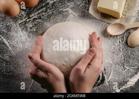 Female hands holding dough. Baking ingredients on the dark wooden table, top view Stock Photo