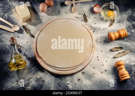 Preparing homemade Italian pizza with a newly rolled dough base surrounded by ingredients for the topping on black background. Top view Stock Photo