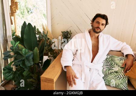 Latin man in white bathrobe rests sitting on couch after baths procedures and wellness at spa resort Stock Photo