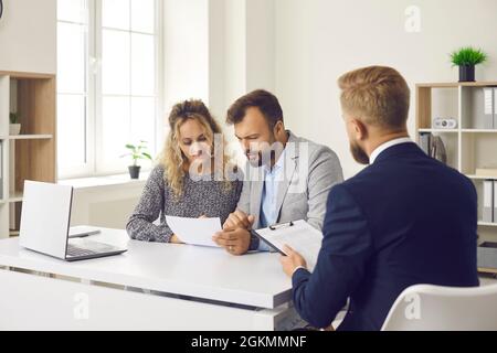 Young couple reading some documents sitting at desk in real estate agent's office Stock Photo