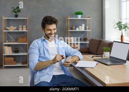 Happy man using cellphone and smiling while sitting at desk with laptop and notebook at home Stock Photo