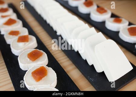 Cottage and goat cheese roller slices with quince jelly, displayed over black slate tray. Closeup Stock Photo