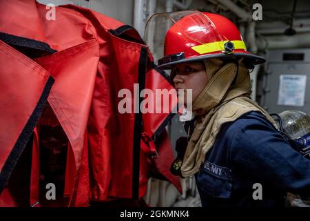 210528-N-XU073-1032  SOUTH CHINA SEA (May 28, 2021) – Machinist’s Mate 3rd Class Leslie Horta, from Los Angeles, dons personal protective equipment during a firefighting drill aboard Arleigh Burke-class guided-missile destroyer USS Curtis Wilbur (DDG 54). Curtis Wilbur is assigned to Commander, Task Force 71/Destroyer Squadron (DESRON) 15, the Navy’s largest forward-deployed DESRON and U.S. 7th Fleet’s principal surface force. Stock Photo