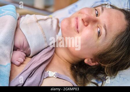 Portrait of a happy mother immediately after a successful birth on the bed in the maternity ward . Laying the child out on the mother chest immediatel Stock Photo