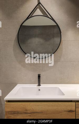 Modern bathroom with white sink, wooden base and round mirror. Minimalist style interior design in warm colors. Stock Photo