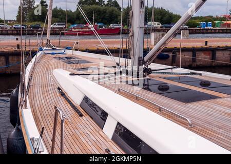 Wooden deck of a large yacht moored in the port of Darłowo, Poland, on the Baltic Sea. Bushes and cars parked on the other side of the harbor canal. Stock Photo