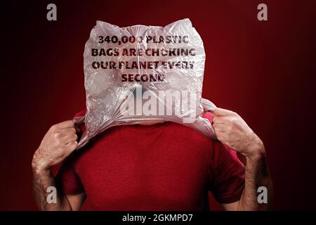 The caucasian man rips off the plastic bag from his head, suffocating. Red background. Copy space. Concept of pollution and environmental protection.. Stock Photo