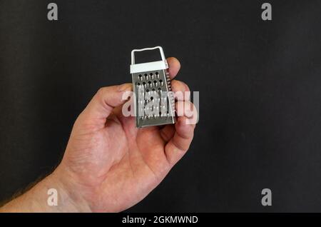 A man's hand holds a miniature metal grater against a dark gray Stock Photo