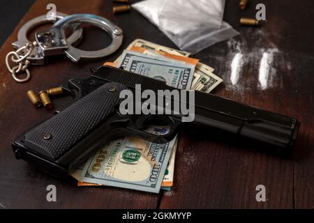 Drugs smuggling and trafficking, Handcuffs, pistol money and cocaine packets on wooden table background. Illegal substances business and arrest Stock Photo