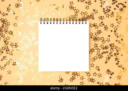 Empty square notebook mockup with glittering stars confetti on a gold background. Stock Photo