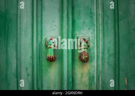 Detail of two rusty door knockers shaped like a woman's hand on vintage green wooden door Stock Photo