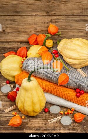 Autumn cozy composition. Ripe pumpkins, warm knitted sweaters, various berries, and candles. Thanksgiving festive greeting card. Old wooden boards bac Stock Photo