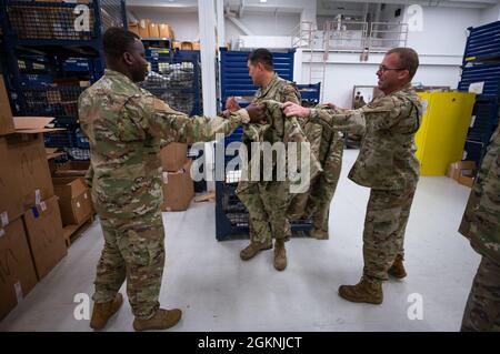 Staff Sergeant Salem Dogbe, Individual Equipment Element, 168th Wing Logistics Readiness Squadron, hands over an Operational Camouflage Pattern cold weather parka to be tried on for size at Eielson Air Force Base, Alaska, June 6th, 2021. Airmen from the 168th Wing, Alaska Air National Guard, are being issued their OCP cold weather parka, a vital part of their uniform when operating in an arctic environment. LRS is tasked with ensuring the Airmen of the 168th Wing are supplied with the clothing and equipment they require for mission success, especially in the sub-zero temperatures of Alaska. Stock Photo