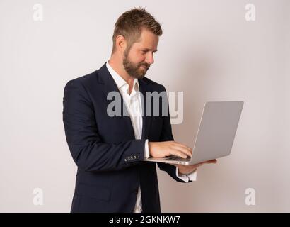 Young business man standing with laptop. Handsome guy holding open notebook in his hand and work on it. Information, technology concept. Stock Photo