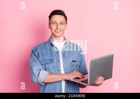 Portrait of young smiling handsome male businessman working in laptop programmer isolated on pink color background Stock Photo