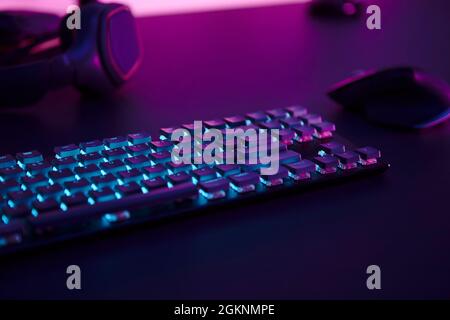 Computer gaming accessories, illuminated keyboard, mouse and headphones laying on desk. Professional computer game playing, esport business and online Stock Photo