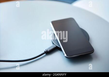 Charging smartphone on round wireless charging pad. Modern technology, wireless device and transfer of energy concept. Stock Photo