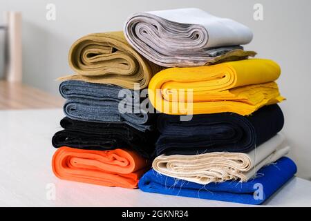Bobbins with threads, measuring tape and stack of colorful fabrics on table. Tailoring accessories Stock Photo